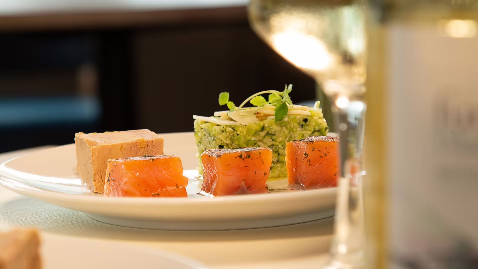 Assiette de saumon fumé et terrine servie avec un verre de vin blanc lors d'un dîner croisière sur la Seine à Paris, offrant une expérience culinaire élégante et raffinée | Le Capitaine Fracasse