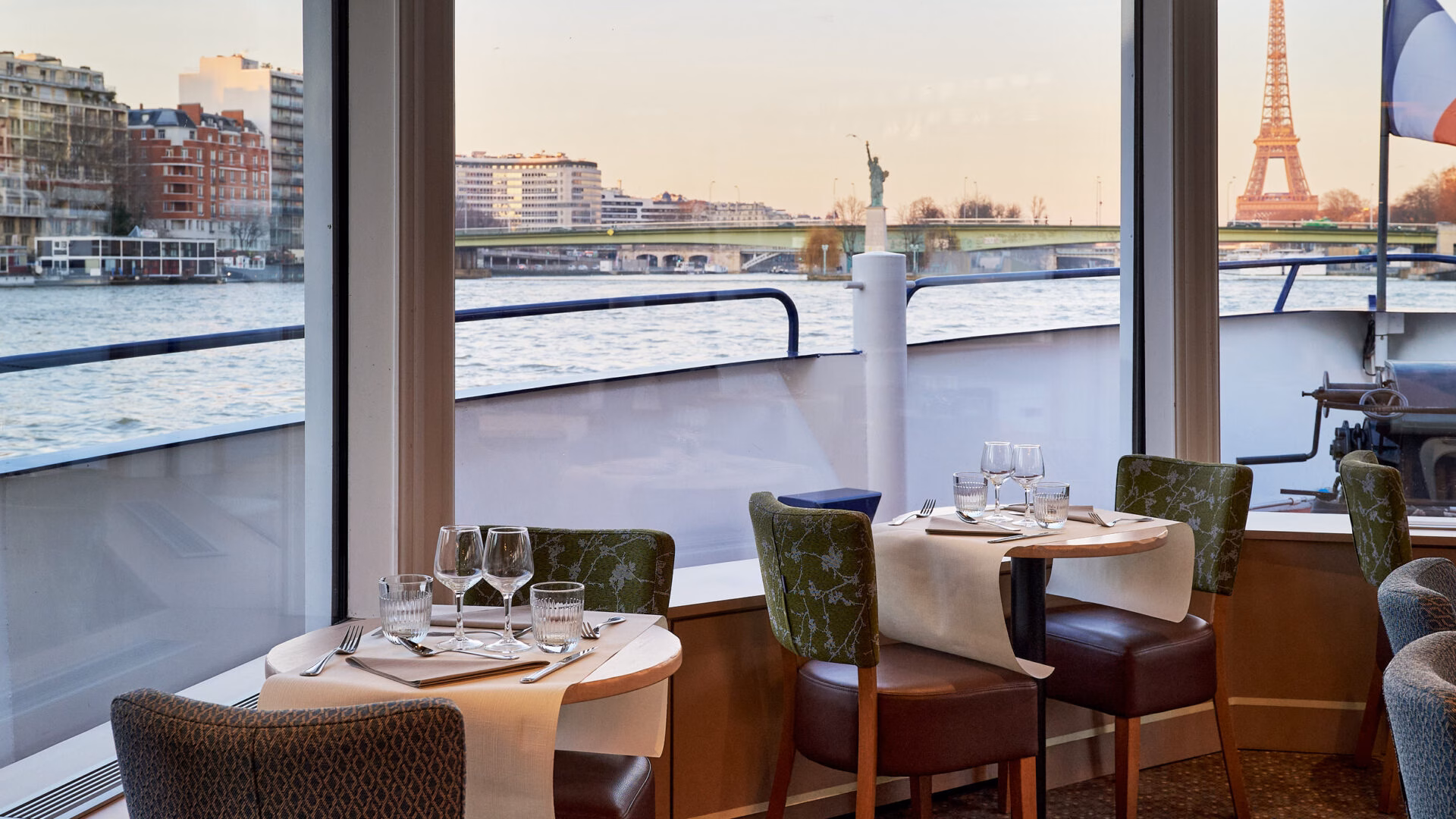 Table élégamment dressée à bord d'un bateau de croisière sur la Seine à Paris, avec vue sur la Tour Eiffel et la Statue de la Liberté parisienne | Le Capitaine Fracasse